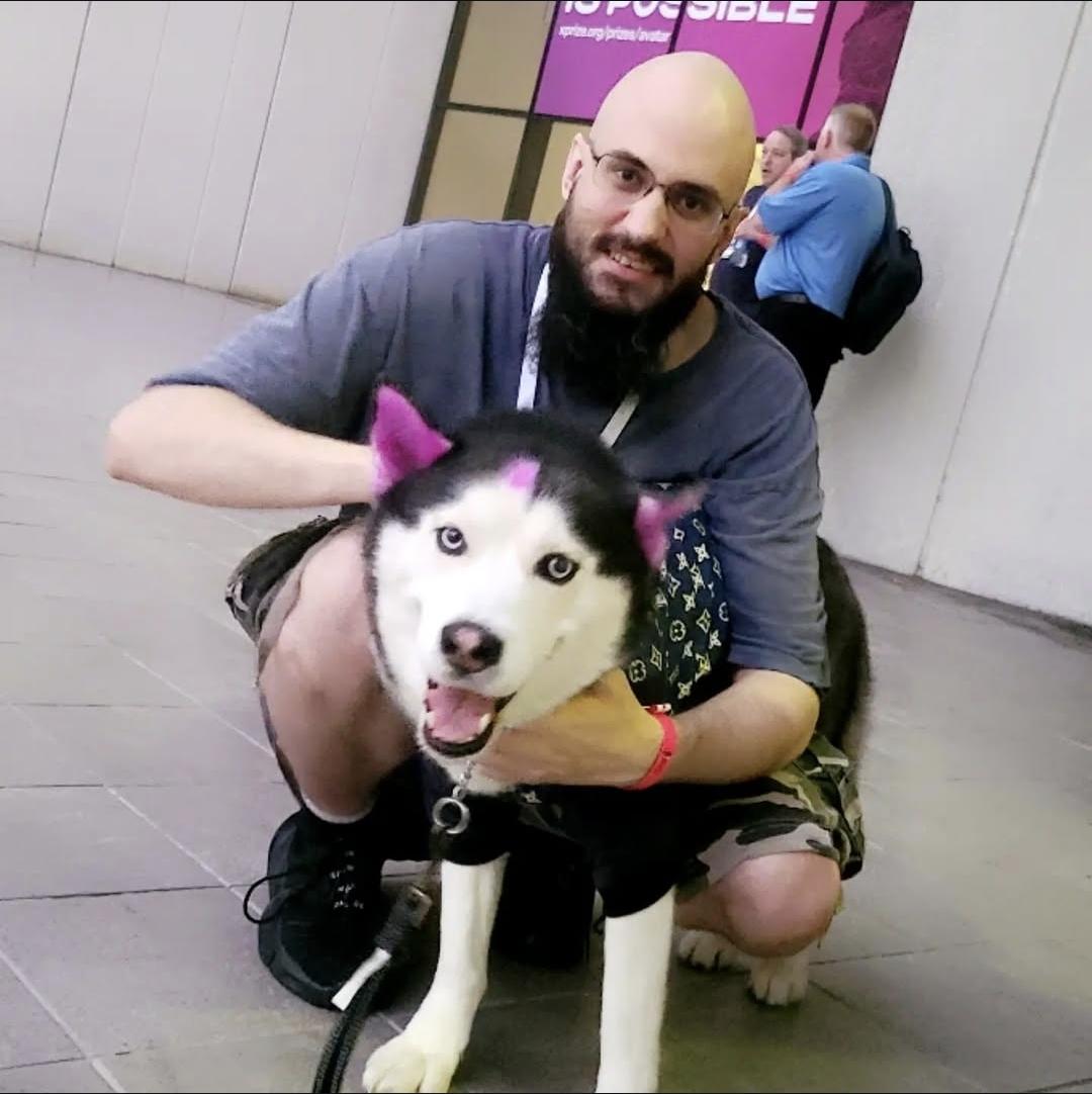 Jeremy Ryan crouching with a black-and-white husky whose ears are dyed pink.