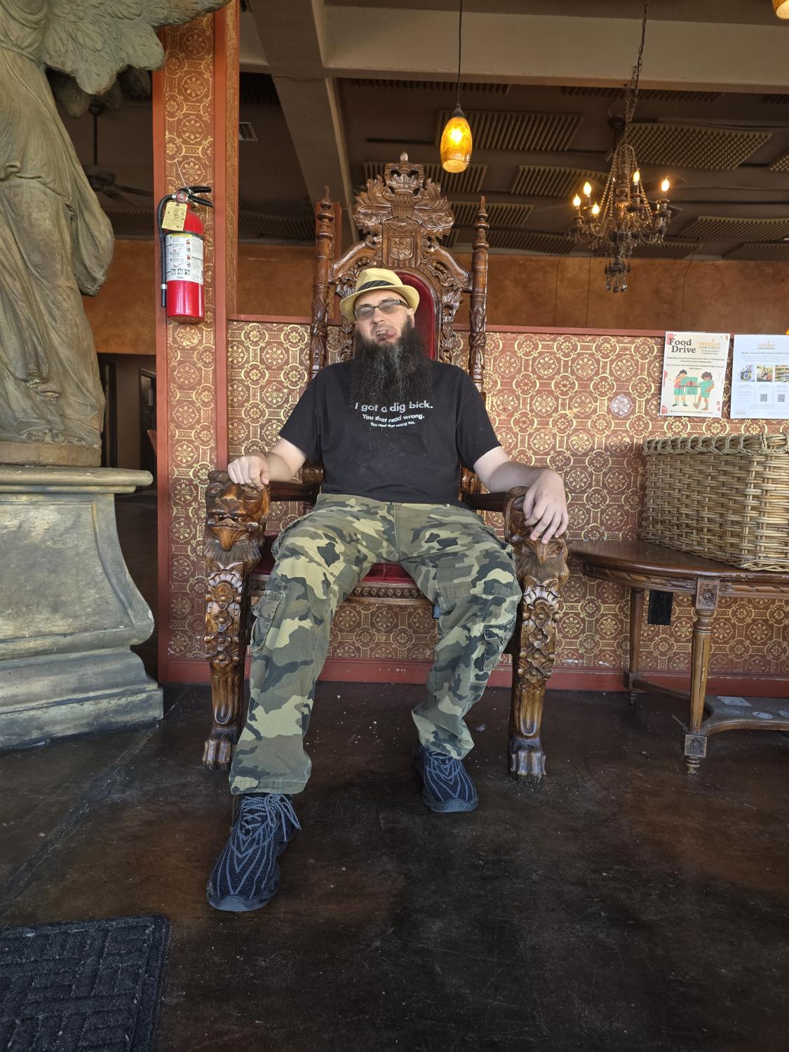 Jeremy Ryan seated on an ornate wooden throne in camouflage pants and a yellow hat.